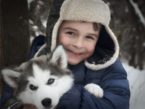 A smiling boy in a winter hat hugging a husky puppy