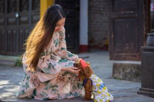 A woman kneeling on a doorstep to greet a small dog